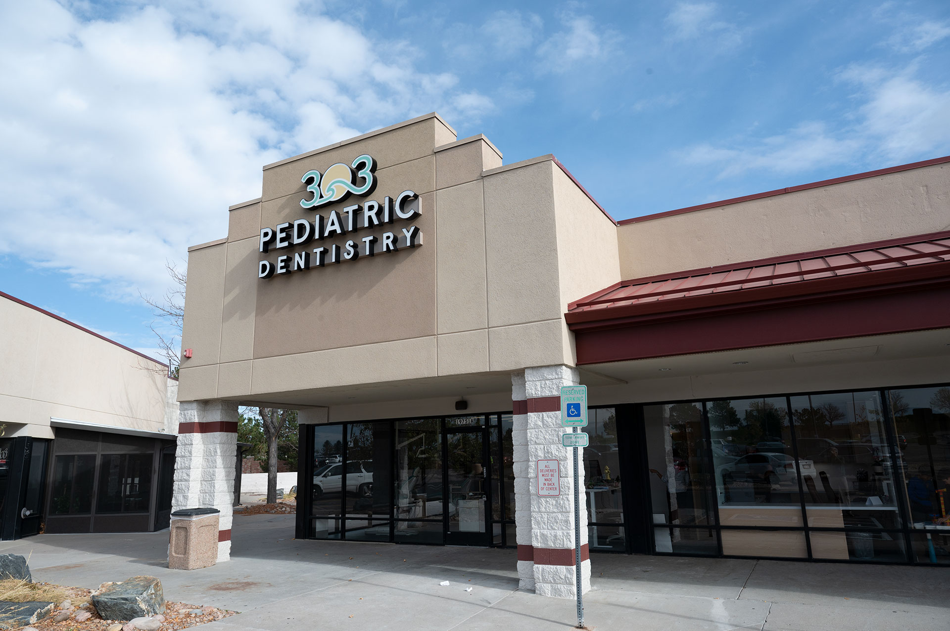 The image shows a building with a sign indicating 303 Pediatric Dentistry and a logo for a dental clinic, situated in a commercial area under a clear sky.